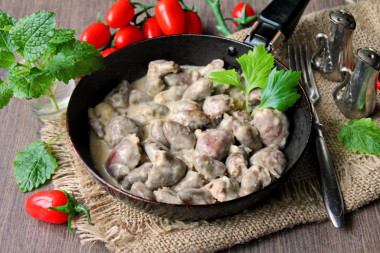 Stewed chicken hearts in sour cream in a frying pan with onions