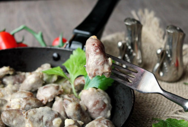 Stewed chicken hearts in sour cream in a frying pan with onions