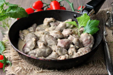 Stewed chicken hearts in sour cream in a frying pan with onions