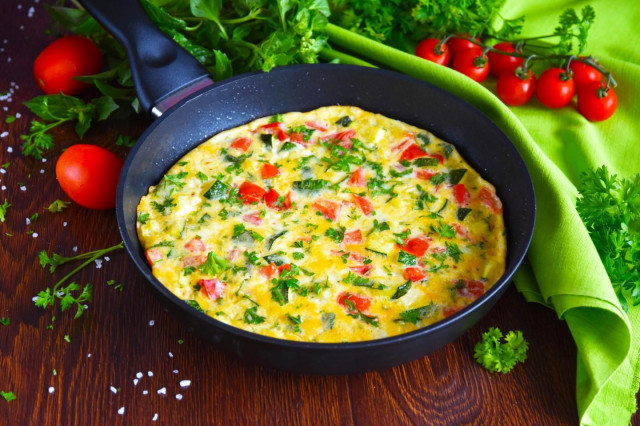Omelet with zucchini and tomatoes in a frying pan