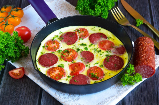 Omelet in a frying pan with sausage and tomatoes