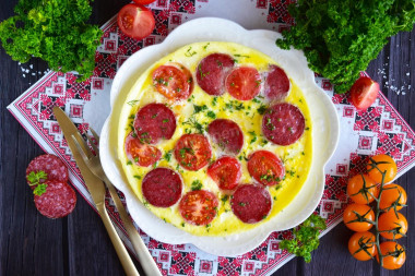 Omelet in a frying pan with sausage and tomatoes