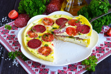 Omelet in a frying pan with sausage and tomatoes