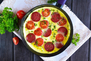 Omelet in a frying pan with sausage and tomatoes