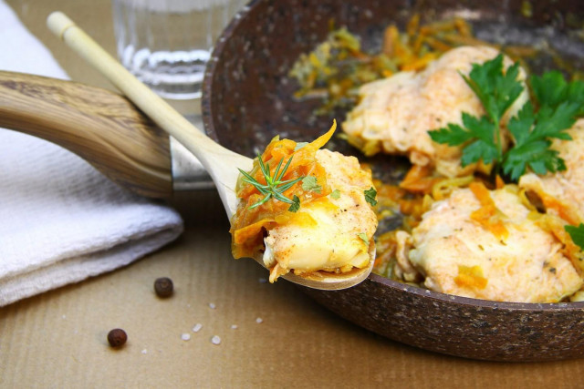 Cod stewed with onions and carrots in a frying pan