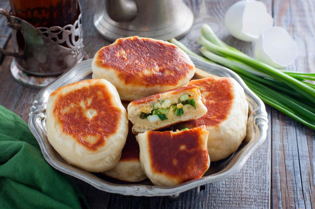 Pies with egg and green onions in a frying pan
